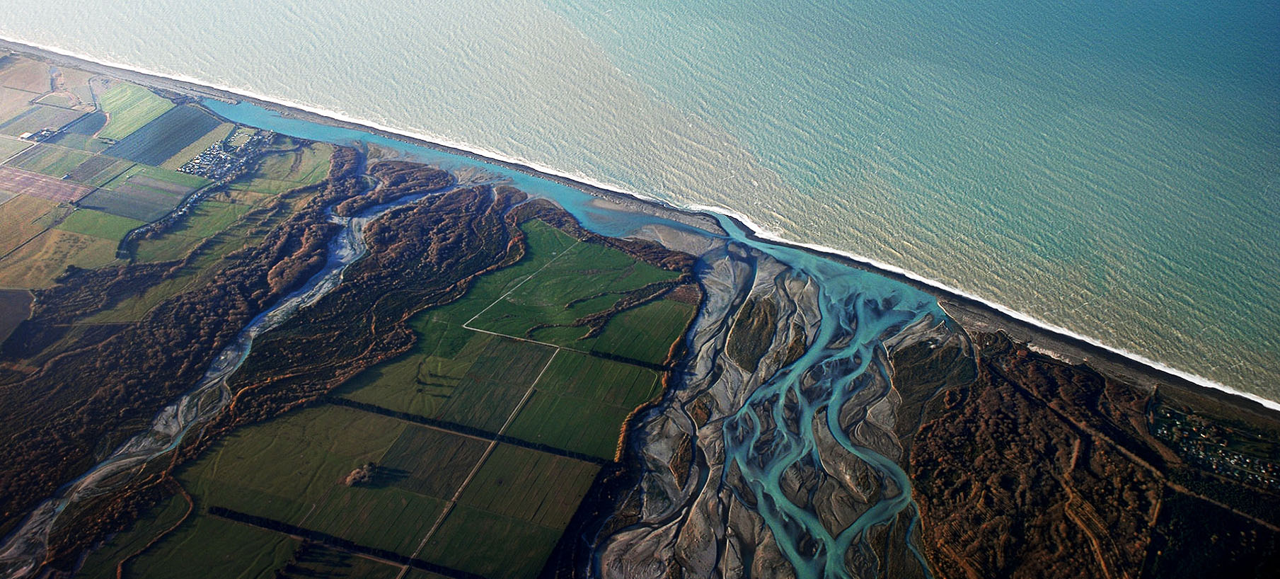 Fig. 1: Rakaia River hapua visible as a long thin blue lagoon along the coast. The northern arm of the Rakaia River flows directly into the hapua, while the Southern (wider) arm also stretches along the coast at the rivermouth before opening to the sea. This configuration is highly dynamic and can change at any time during storms or floods. (Image: Phillip Capper | Wikipedia Commons)